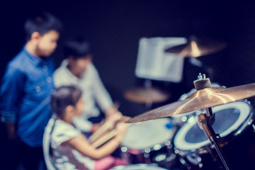 Fototapeta na wymiar Selective focus to cymbals of drum set with blurry kid learning and play drum set with teacher in music room. The concept of musical instrument.