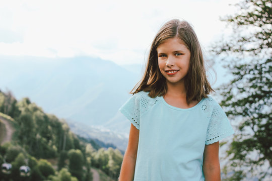 Smiling tween girl looking at camera on the background of beautiful mountains, family travel concept adventure lifestyle