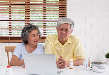 Asian couple seniors use laptop video conference with doctor about illness and prescription pill in living room at home.Healthy lifestyle.aging at home concept