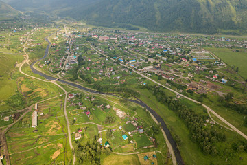 Panorama of the mountains with small village  in Altai on a summer clear day. A landscape view of beautiful fresh green field   and  Altai mountain background.  Panoramic view of beautiful green field