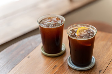 Two cup of Lemon slices in Iced cold brew coffee on wooden table.