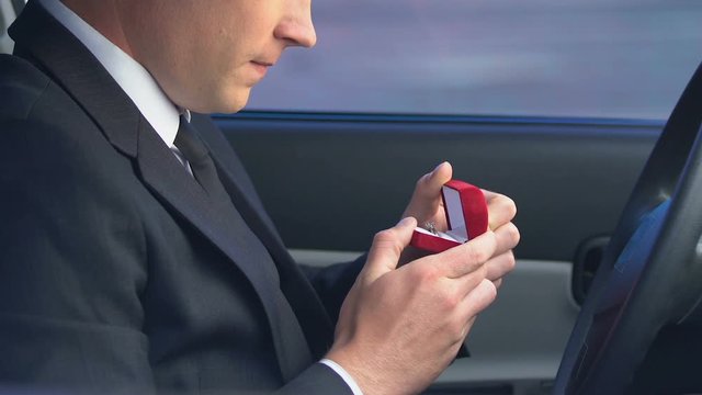 Insecure man holding wedding ring sitting in car, overcoming engagement anxiety