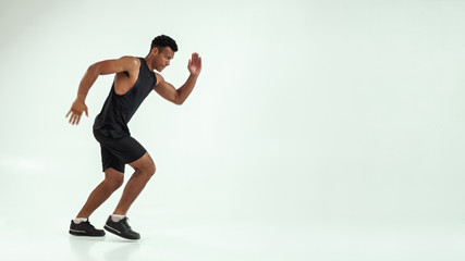 Full length of young african man with muscular body in sports clothing preparing to run in studio against grey background