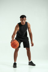 Great game. Full length of young african man in sports clothing playing basketball in studio against grey background