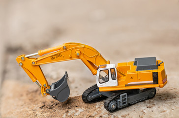 Yellow excavator model toy performs excavation work on a construction site. (Image stacking technique)