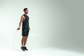 New champion. Full length of young african man in sport clothing skipping rope while exercising in studio against grey background