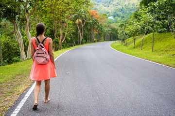 Beautiful rainforest with a young woman traveler with a backpack on the road to the forest Thailand. A woman walks along a tropical road and enjoys the views of nature.