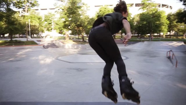 Slender young man in casualclothes riding on inline roller skates at ramp in public skate park, makes a jump and hangs in a time. Spring, summer time. Slow motion