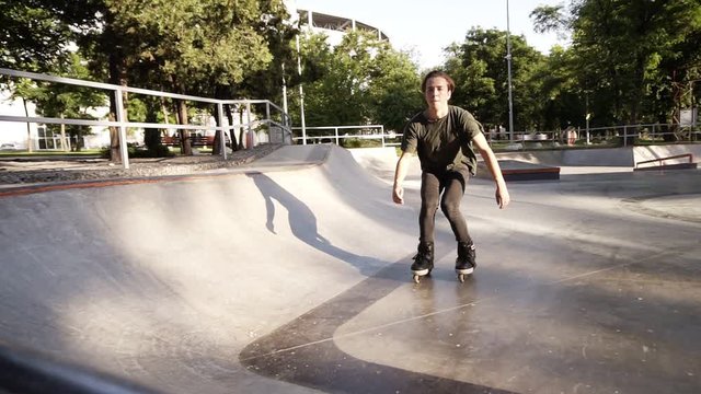 Inline roller skater doing tricks in concrete skatepark outdoors with beautiful green park background, slow motion. Close up footage on the top of the ramp