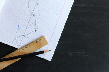 simple pencils and a wooden ruler on the background graphics of the function in a notebook and school blackboard top view. taking notes on physics classes