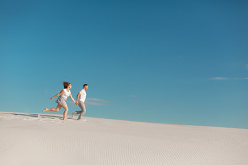 Fototapeta premium Romantic couple in love running on white sand in desert