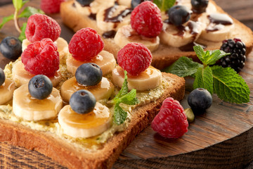 Sandwiches with banana, raspberry blueberry, blackberry and blueberry on bread with honey and chocolate and mint on a wooden table