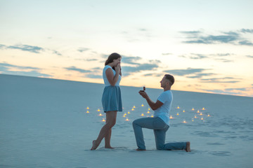 The guy makes the girl a marriage proposal by bending his knee while standing on the sand in the...