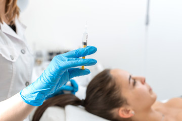 The beautician holds a syringe with an rejuvenation injection on the background of the patient. A...