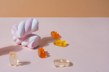 Sweets minimalistic pastel bright cute background with negative space marshmallows and gummy bears on pink and beige pastel background
