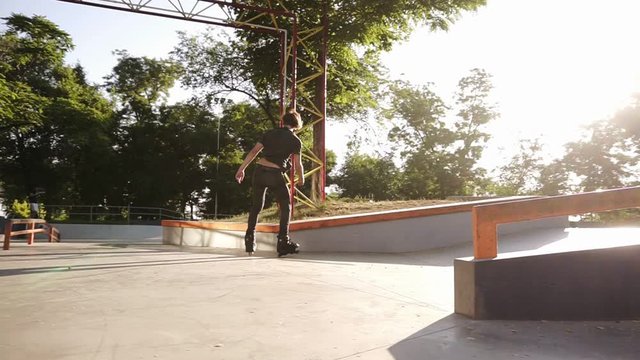 A young athlete performs a hard trick on rollers - jumps through the railings, doing double turn toe loop and bend his legs in the air. Slow motion. Outdoors skate park