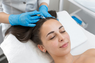 Obraz na płótnie Canvas Beautician injections for healthy hair growth. Mesotherapy of the scalp. A young girl is undergoing a course of spa treatments in the office of a beautician. Moisturizing