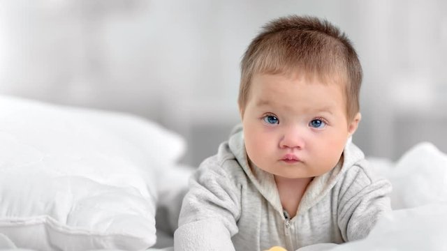 Portrait of pretty innocence little baby with blue eyes posing at white bedroom interior