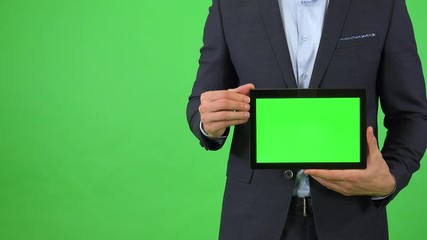 A businessman in a suit holds out a tablet with green screen - closeup - green screen studio