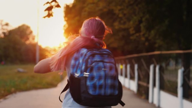 A girl with a schoolbag behind her runs along the alley to the school in the sun. Back to school