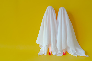 Two girl dolls cover with white sheet costume on yellow background. Minimal Halloween scary concept.
