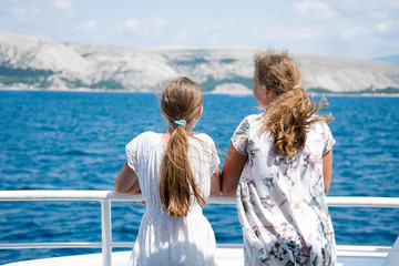 Fototapeta na wymiar Two girls stand at deck of ship and look at the ocean and island, Croatia.