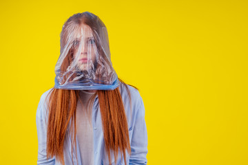 redhaired ginger european woman suffocation head in blue polyethylene package in studio yellow...