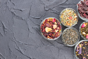 Obraz na płótnie Canvas Tea types on black stone background. Assortment of dried tea on slate with text space. Herbal tea health benefits.