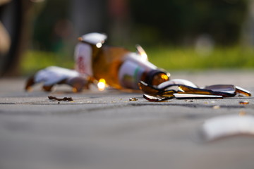 bottle of beer, soda or drugs from dark glass is broken. Shattered beer bottle on ground in sunset light. Fragments of glass on asphalt. Texture, background, wallpaper.