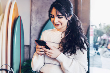 Portrait of girl sitting cafe, using smartphone. Young woman reads text message on phone while sitting coffee shop. Lifestyle.