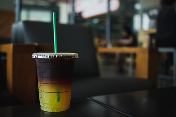Takeaway cup of ice coffee with orange juice on table in cafe
