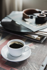 White cup of coffee with vinyl records and headphones on table in living room