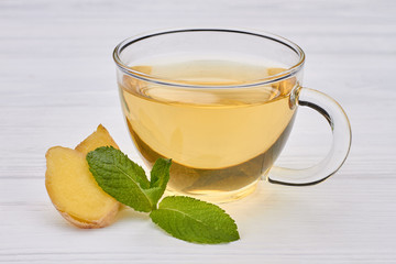 Cup of tea with ginger and mint. Glass transparent cup of green tea with ginger and mint leaves on wooden background. Healthy drink and diet concept.