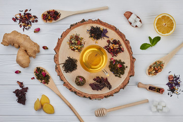 Flat lay composition with different kinds of dry tea. Glass cup of tea, lemon, ginger, mint and assorted dry tea on wooden background.