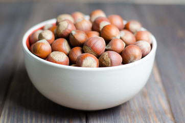 Hazelnuts in a white plate. Brown wooden background. Selective focus