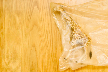 Concept for plastic pollution, environmental pollution, ecology problem. The figurine of a giraffe in a polyethylene bag. Children's toy. Flat lay, top view