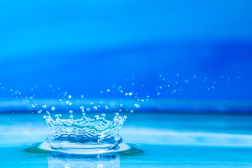 Naklejka na ściany i meble close up of a water drop impacting a body of water on a blue background