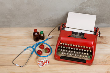 Prescription medicine or medical diagnosis - doctor workplace with blue stethoscope, pills, red typewriter, strawberries