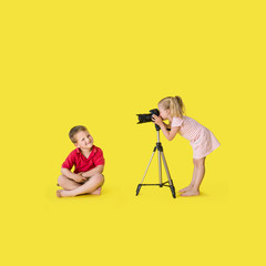 Little boy and girl play in photographer and model on yellow background