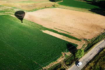 Balloon flight above the cultivated fields, shadow of the hot air balloon flying in the sky.