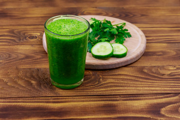 Glass of green detox smoothie of cucumber and parsley on a wooden table
