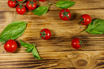 Fresh cherry tomatoes with green basil leaves on a wooden table. Top view