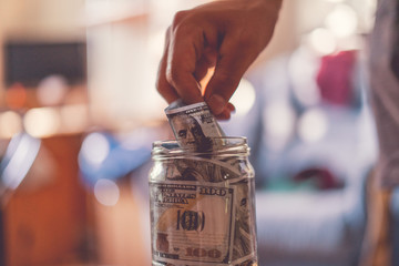 hand put some money in the glass bank with savings