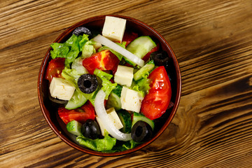 Greek salad with fresh vegetables, feta cheese and black olives on wooden table. Top view