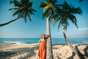 Vacation concept, happy young woman smiles, in the summer against a backdrop of palm trees and ocean. Portrait of carefree girl  joy and laughing while standing  near palm tree