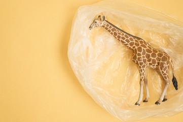 Concept for plastic pollution, environmental pollution, ecology problem. The figurine of a giraffe in a polyethylene bag. Children's toy. Flat lay, top view