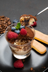 Classic tiramisu dessert portion with blueberries and raspberries in a glass cup on stone serving board on concrete background