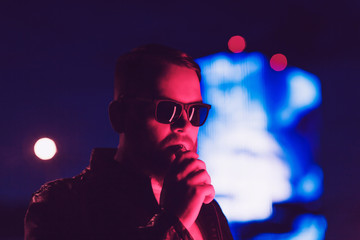 Man with beard in sunglasses holding vape. night portrait