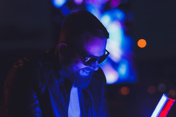 Naklejka premium Neon portrait of smiling man model with beard in sunglasses and leather jacket