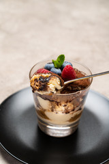 Classic tiramisu dessert portion with blueberries and raspberries in a glass cup on concrete background